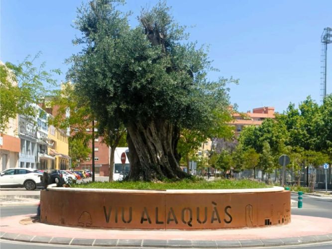 Escultura de acero corten oxidado en la rotonda del Olivo en Alaquas vista de los edificios historicos